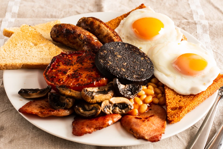 A plate of a traditional Full English Breakfast with sausages, bacon, eggs, black pudding, grilled tomato, mushrooms, baked beans, and toast.